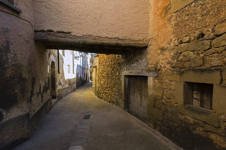 Callejuela estrecha de piedra con un pasadizo bajo una casa en un pueblo antiguo, lugar que solo se descubre al viajar despacio